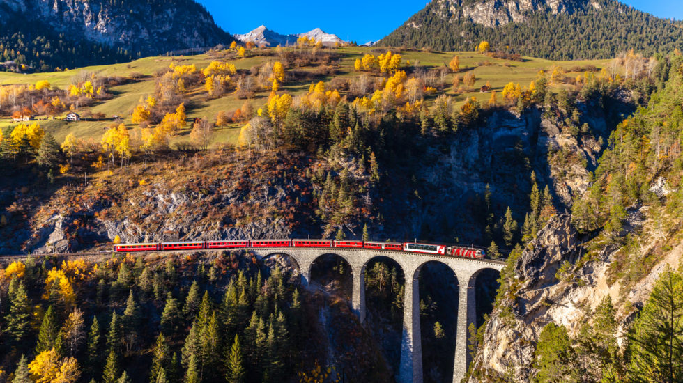 The Train Of  Rhaetian Railway Running On The Famous Landwasser Viaduct Into The Tunnel, With View Of Colorful Trees On A Sunny Autumn Day, Canton Of Grisons, Switzerland