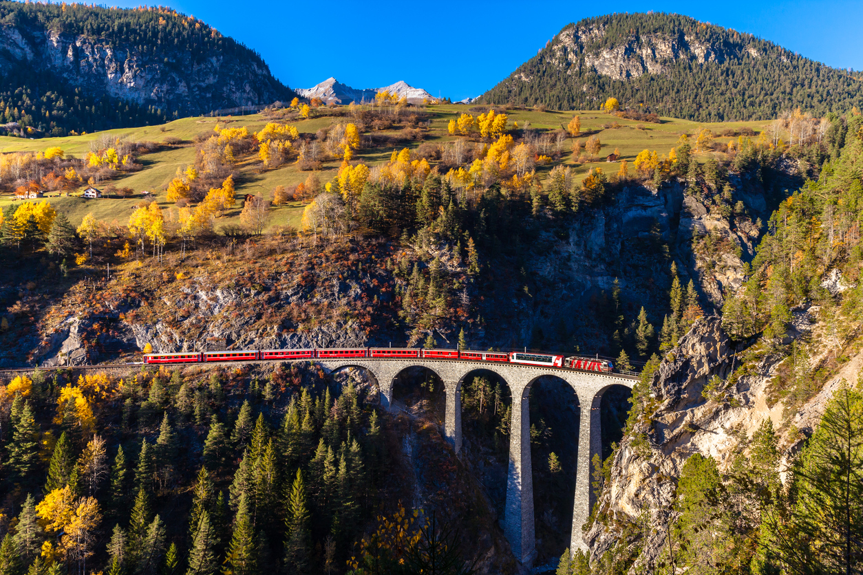 The Train Of  Rhaetian Railway Running On The Famous Landwasser Viaduct Into The Tunnel, With View Of Colorful Trees On A Sunny Autumn Day, Canton Of Grisons, Switzerland